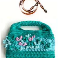 Sac à main au crochet fait main en coton vert et celadon, orné de fleurs en relief, avec poignée intégrée, sur fond blanc. Bandoulière amovible et réglable en cuir cognac.