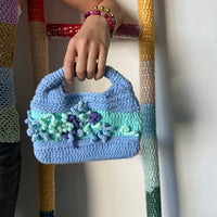 femme debout portant un haut en crochet Anabaum et à la main le sac en crochet Anabaum Bleu Ciel dans les tons Bleu ciel céladon , texturé comme du corail