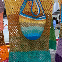 Paris Designed Handmade crochet dress and matching bag set featuring an open mesh knit and gradient colors from yellow to blue, with a striped crochet bucket bag and blue shoulder strap, displayed indoors.