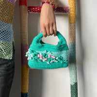 femme debout portant un haut en crochet Anabaum et à la main le sac en crochet Anabaum corail vert dans les tons vert et celadon, texturé comme du corail