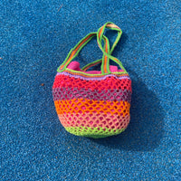 Flat lay of the Lil Sis Funky handmade crochet bag on a blue towel, multicolor neon stripes in green, pink and orange, designed in Paris by Anabaum