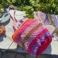 sac crochet dans les roses parme doré et rouge posé sur un mur de pierres ensoleillé