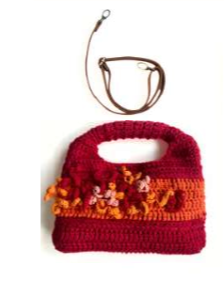 Sac à main au crochet fait main en coton rouge et orange orné de fleurs en relief multicolores, avec poignée intégrée, sur fond blanc.

Bandoulière en cuir cognac amovible et réglable