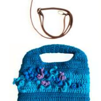Sac à main au crochet fait main en coton bleu canard et turquoise, orné de fleurs en relief multicolores, avec poignée intégrée, sur fond blanc.

Bandoulière en cuir cognac amovible et réglable