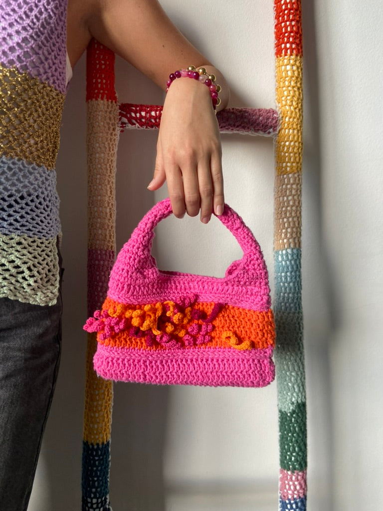 femme debout portant un haut en crochet Anabaum et à la main le sac  en crochet Anabaum corail Rose dans les tons fuschia et orange, texturé comme du corail 