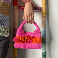 femme debout portant un haut en crochet Anabaum et à la main le sac  en crochet Anabaum corail Rose dans les tons fuschia et orange, texturé comme du corail 