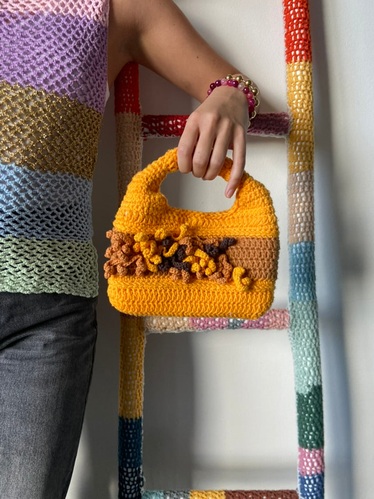 femme debout portant un haut en crochet Anabaum et à la main le sac  en crochet Anabaum Corail Jaune dans les tons jaune d'or et marron , texturé comme du corail 