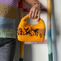 femme debout portant un haut en crochet Anabaum et à la main le sac  en crochet Anabaum Corail Jaune dans les tons jaune d'or et marron , texturé comme du corail 