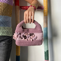 femme debout portant un haut en crochet Anabaum et à la main le sac  en crochet Anabaum Corail Parme dans les tons parme et rose pale , texturé comme du corail 