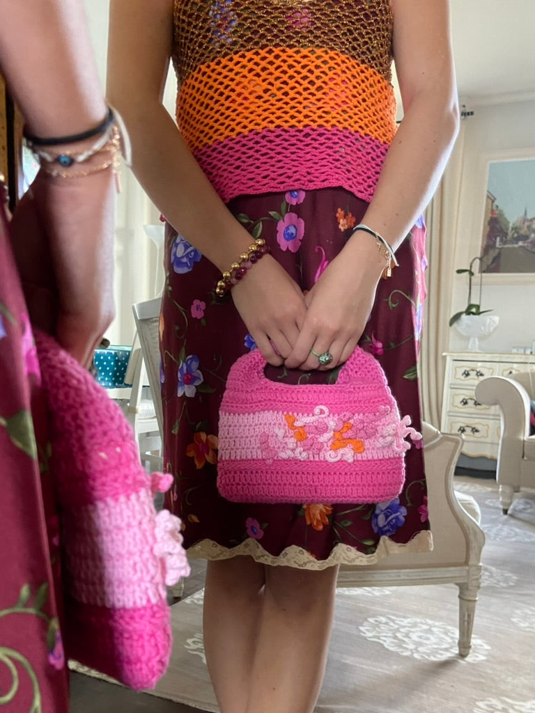 femme debout en tenue habillée d'une jupe en soie et un haut en crochet Anabaum portant à la main le sac anabaum corail Rose dans les tons fuschia et rose pale, texturé comme du corail