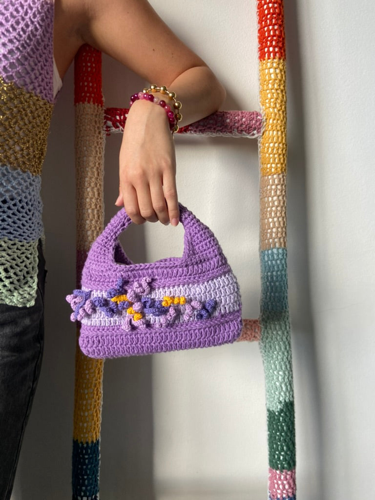 femme debout portant un haut en crochet Anabaum et à la main le sac  en crochet Anabaum corail Violet et lilas texturé comme du corail 