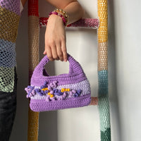 femme debout portant un haut en crochet Anabaum et à la main le sac  en crochet Anabaum corail Violet et lilas texturé comme du corail 