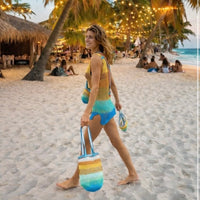 Woman walking on a sandy beach at sunset wearing a crochet bikini top and carrying the OG Sirena crochet bag