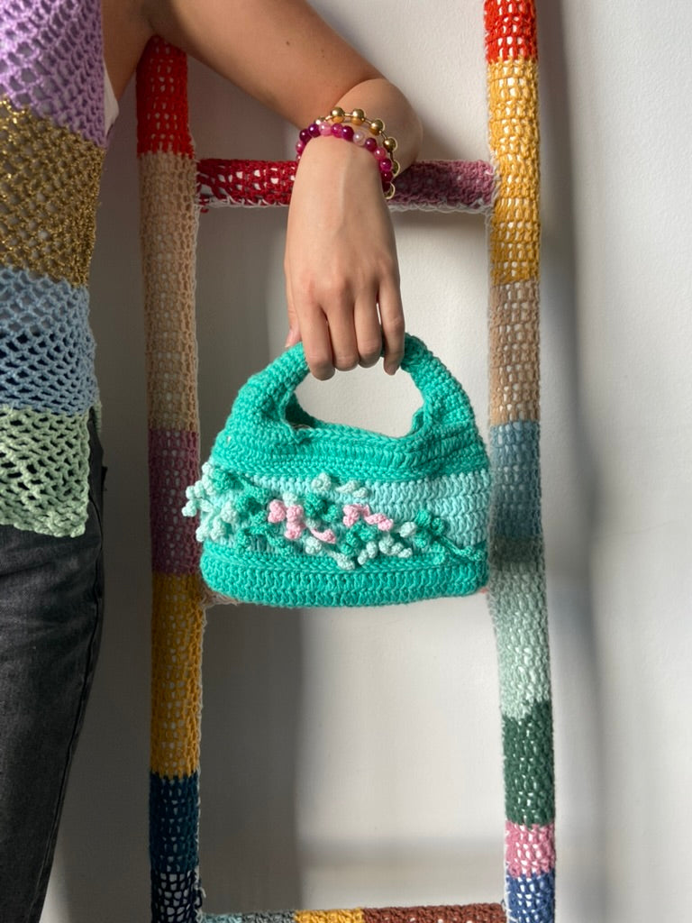femme debout portant un haut en crochet Anabaum et à la main le sac  en crochet Anabaum corail vert dans les tons vert et celadon, texturé comme du corail 
