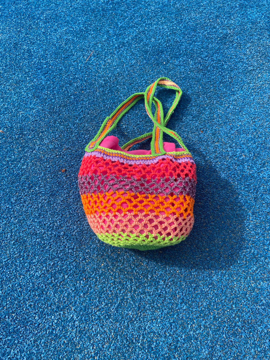 Flat lay of the Lil Sis Funky handmade crochet bag on a blue towel, multicolor neon stripes in green, pink and orange, designed in Paris by Anabaum