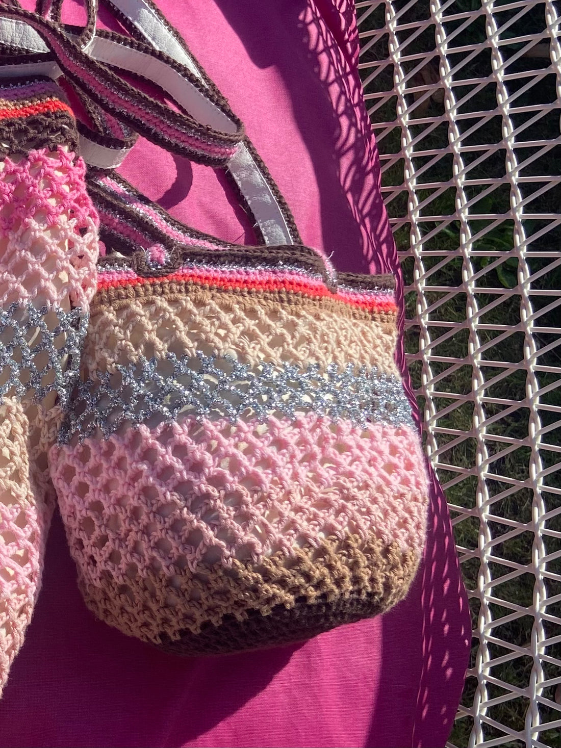 Close-up of the Lil Sis Sandstorm handmade crochet bag in pink, mauve and grey stripes, resting on a wicker chair with a fuchsia background