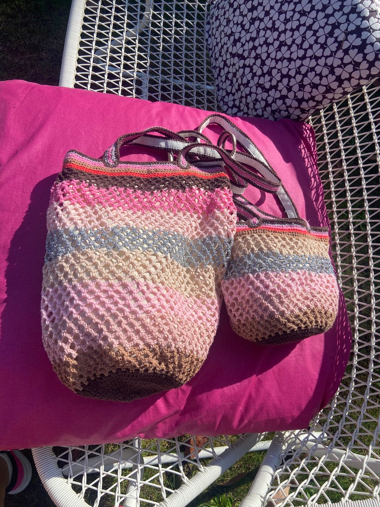 Two Sandstorm handmade crochet bags , one OG , one Lil SIs, resting on a wicker chair with a fuchsia cushion, showcasing the pastel pink, silver and brown colorway