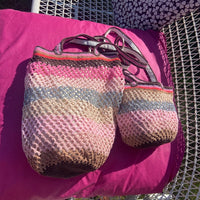 Two Sandstorm handmade crochet bags , one OG , one Lil SIs, resting on a wicker chair with a fuchsia cushion, showcasing the pastel pink, silver and brown colorway