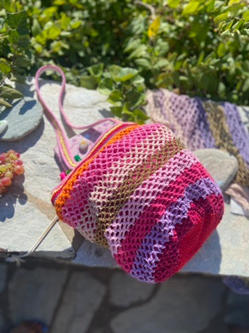 sac crochet dans les roses parme doré et rouge posé sur un mur de pierres ensoleillé