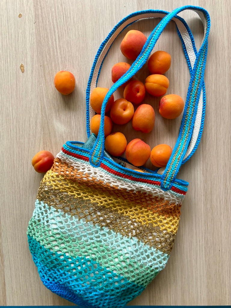 anabaum OG Sirena crochet market bag filled with apricots, laid flat on a wooden surface with blue handles
