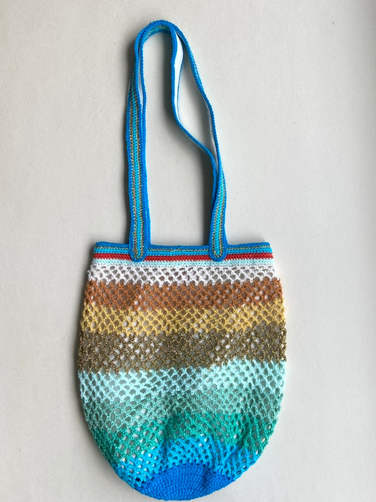 Flat lay of the OG Sirena handmade crochet bag with a blue handle and gradient color pattern on a white background