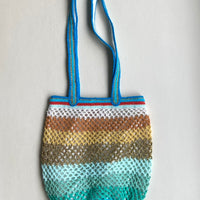 Flat lay of the OG Sirena handmade crochet bag with a blue handle and gradient color pattern on a white background