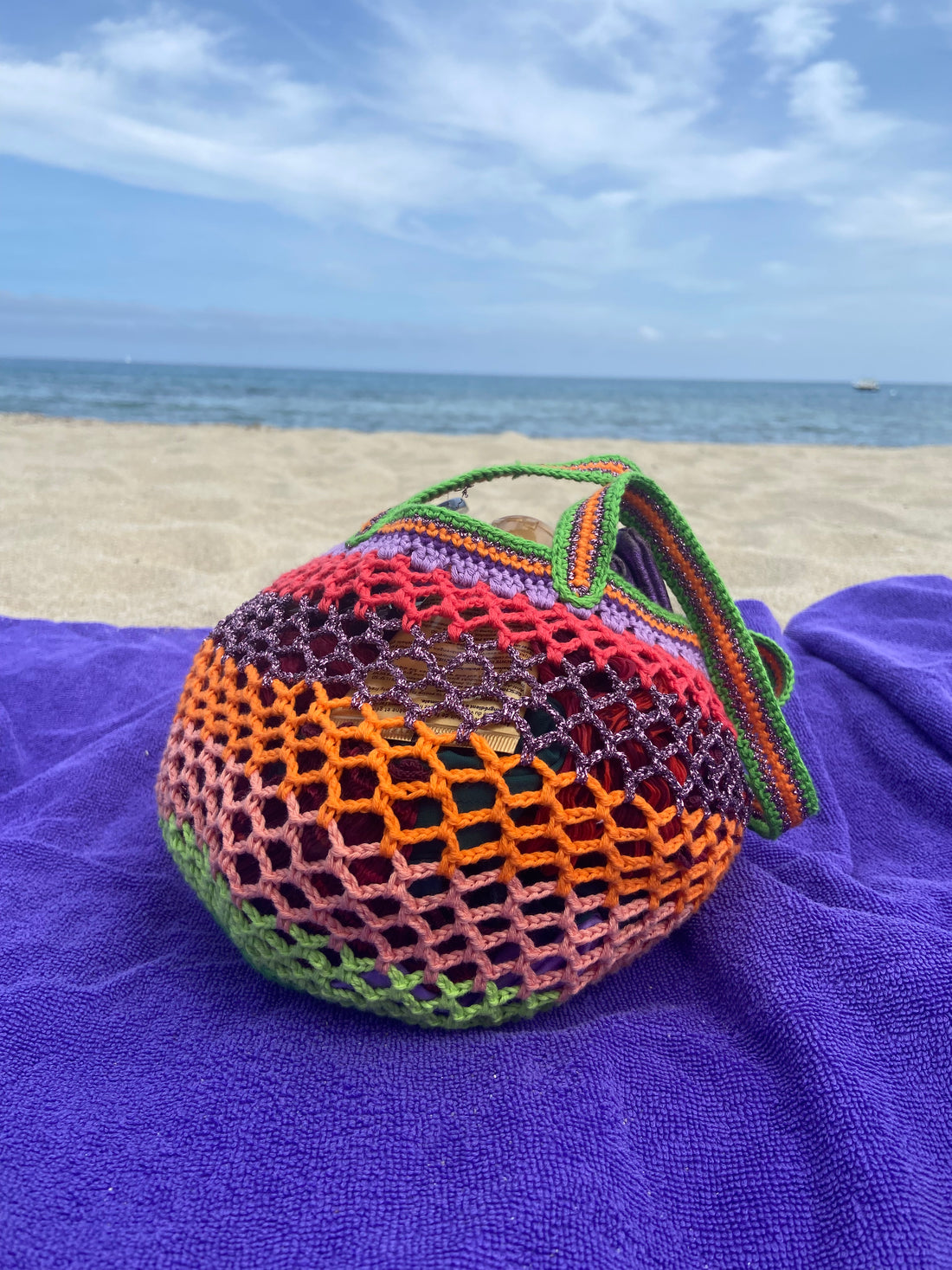 Lil Sis Funky crochet bag resting on a purple beach towel with ocean in the background, bold neon colorway, designed in Paris by Anabaum