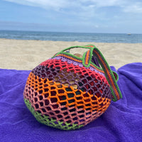 Lil Sis Funky crochet bag resting on a purple beach towel with ocean in the background, bold neon colorway, designed in Paris by Anabaum